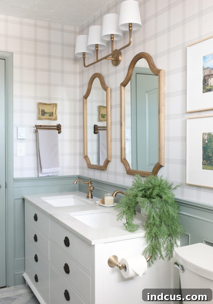 White vanity, plaid wallpaper, wood mirrors, gold hardware and light fixture, antique cabinet pulls in a newly renovated bathroom