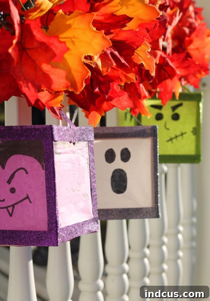 Multiple DIY Halloween luminaries, featuring ghost and monster faces, hanging from a porch railing with a Fall leaf garland.