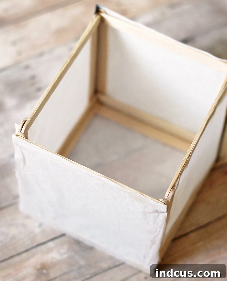 Several craft stick and tissue paper panels glued together, forming an open-sided cube structure for a luminary.