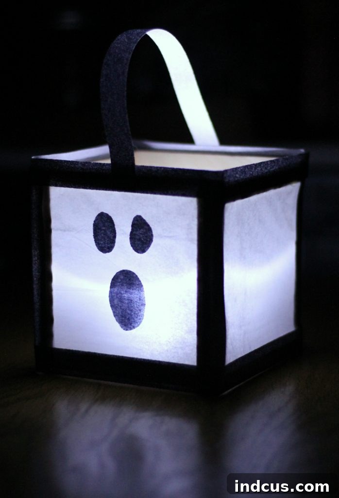 A finished DIY Halloween luminary glowing from within, displaying a ghost face, placed on a dark surface.