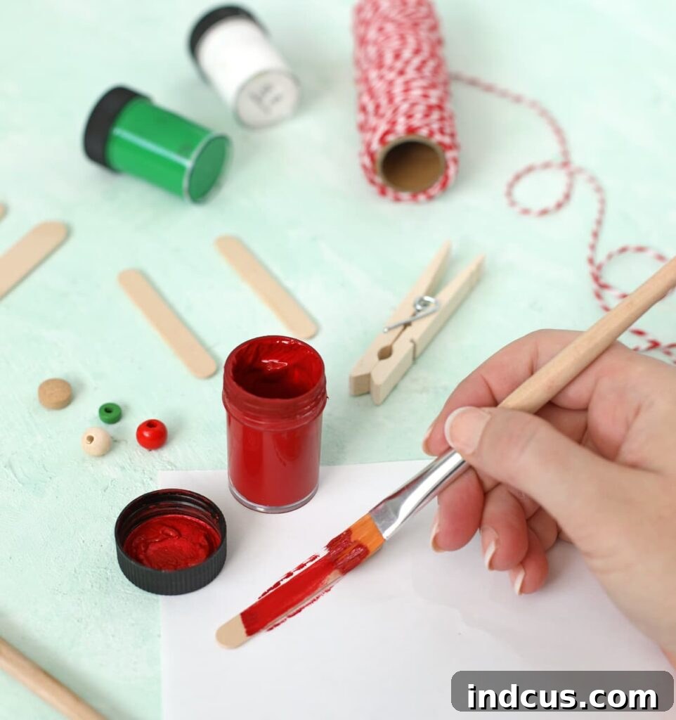 Child's hands painting popsicle sticks in various colors for the airplane ornament