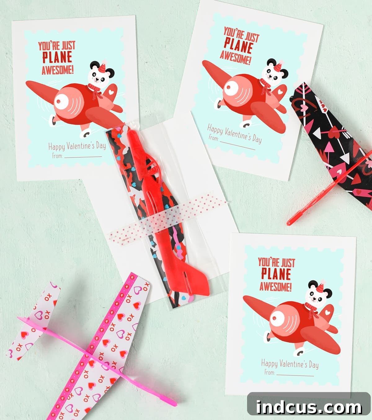 Close-up of a printable airplane Valentine's Day card featuring a cute panda pilot, with a plastic glider plane attached to the back using washi tape.