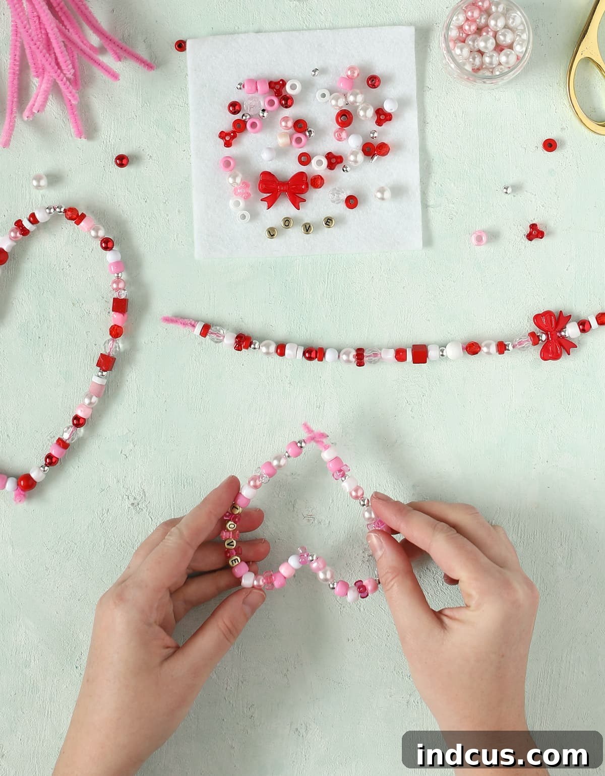 Child stringing colorful beads onto a pipe cleaner to create a beaded heart craft.