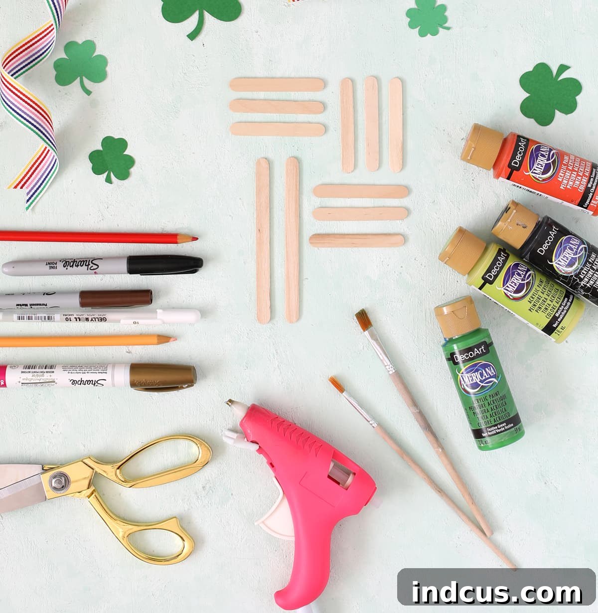 A flat lay photograph showcasing all the materials needed to craft popsicle stick leprechauns, including craft sticks, paint, brushes, and paint pens.