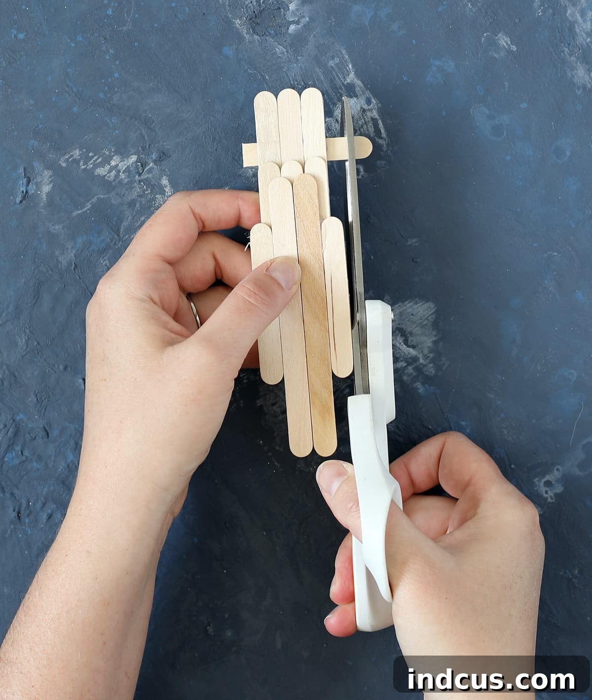 Scissors trimming the ends of craft sticks for a patriotic craft, demonstrating an optional step for refinement