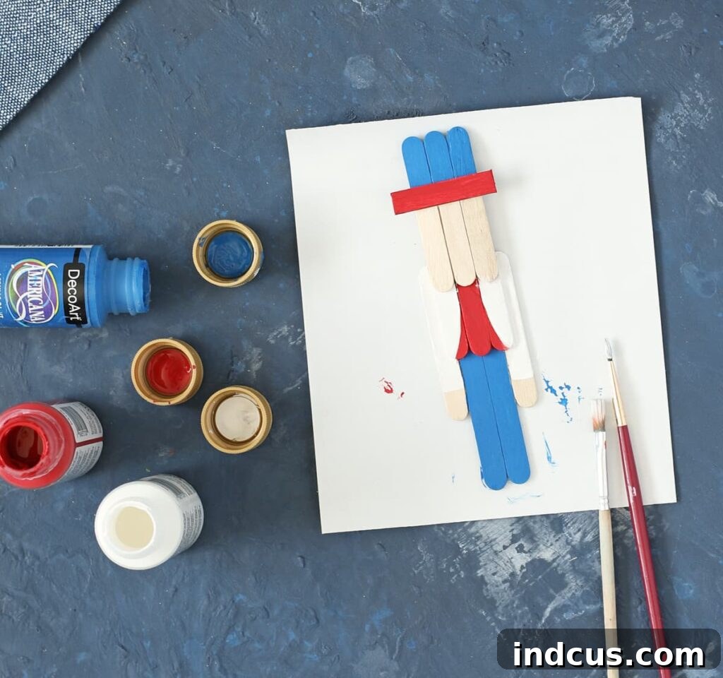 Popsicle stick craft figures partially painted with base colors, showing red, white, and blue sections