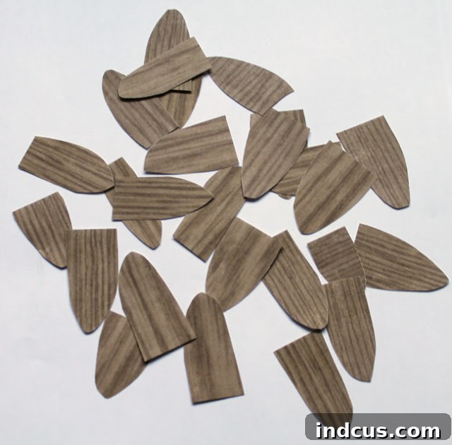 Close-up of numerous small, leaf-shaped paper cutouts with a wood grain pattern, meticulously prepared for crafting a beautiful cone Christmas tree