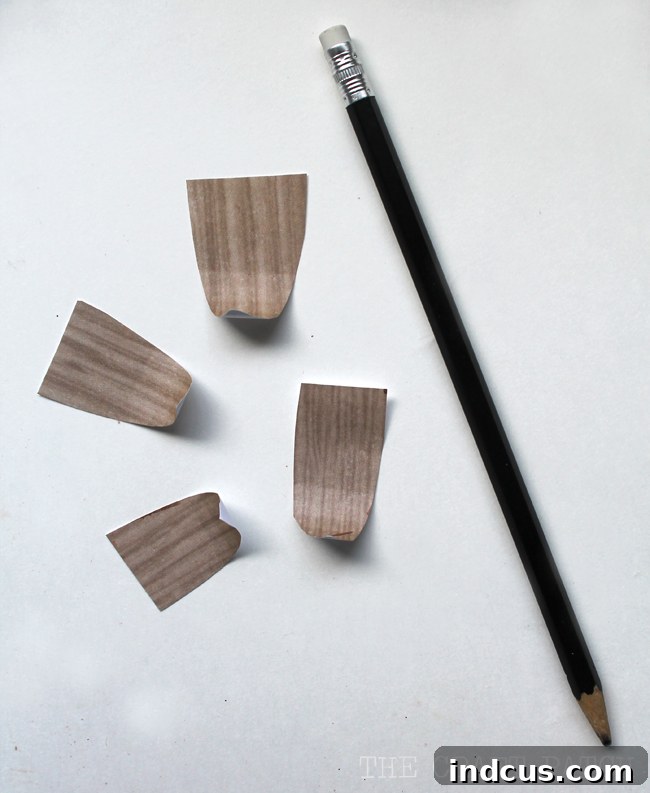 A hand demonstrating the technique of curling a wood-patterned paper leaf around a pencil to add texture and shape for the DIY Christmas cone tree