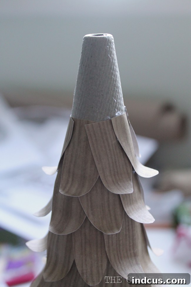 A cone form partially covered with overlapping wood-patterned paper leaves, showcasing the meticulous layering process of the DIY Christmas tree