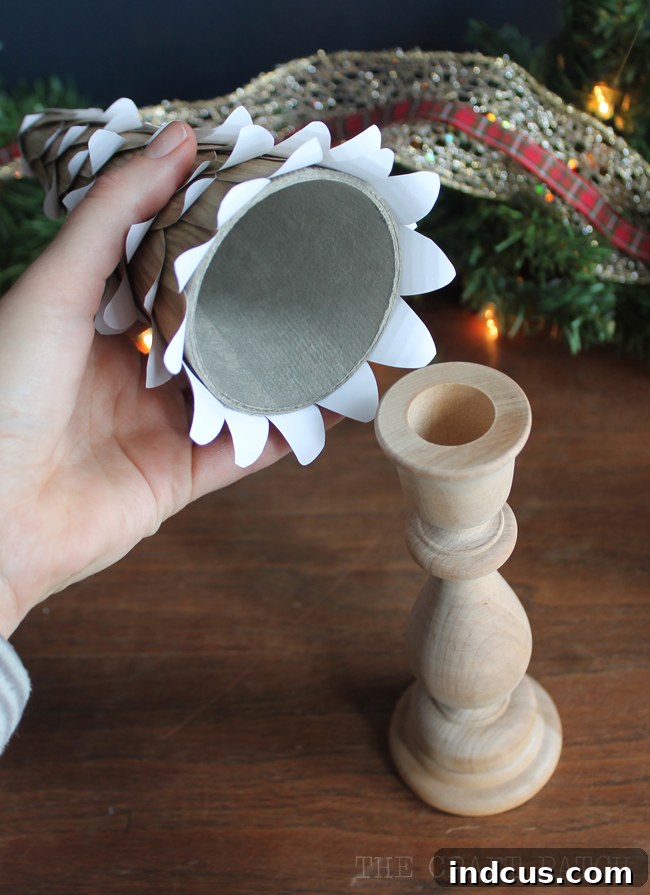 A completed paper cone tree being securely attached to a wooden candlestick base with hot glue, illustrating the final assembly step for a stable DIY Christmas decoration