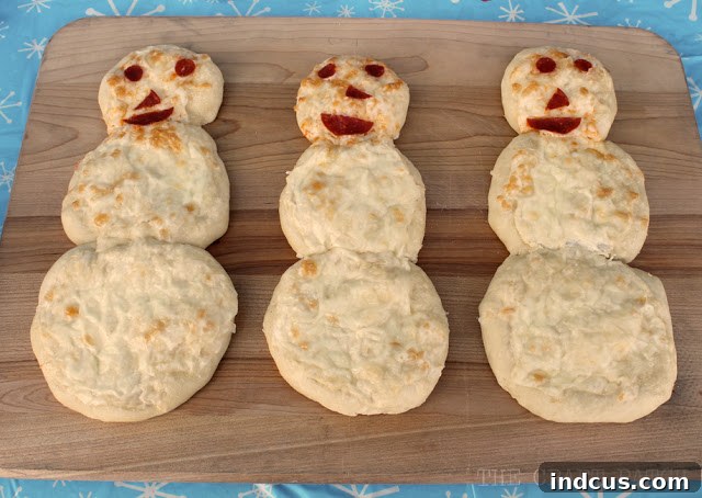 Delicious mini snowman pizzas, expertly shaped from dough and generously topped with savory white sauce and classic pepperoni, ideal for a winter party.