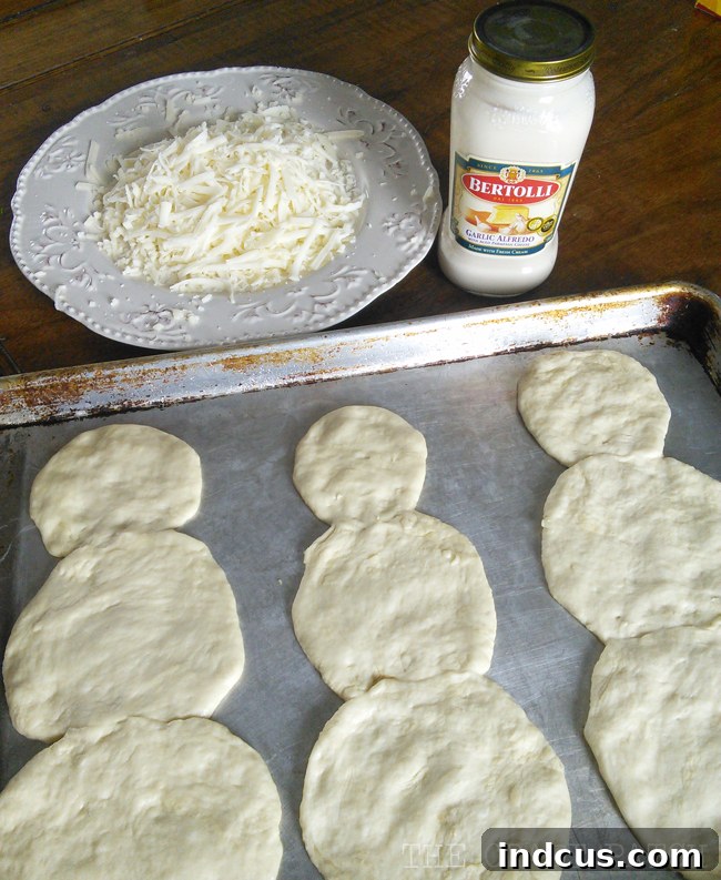 Snowman shaped pizza dough base, beautifully topped with creamy white alfredo sauce and a generous layer of delicious mozzarella cheese, ready for toppings.