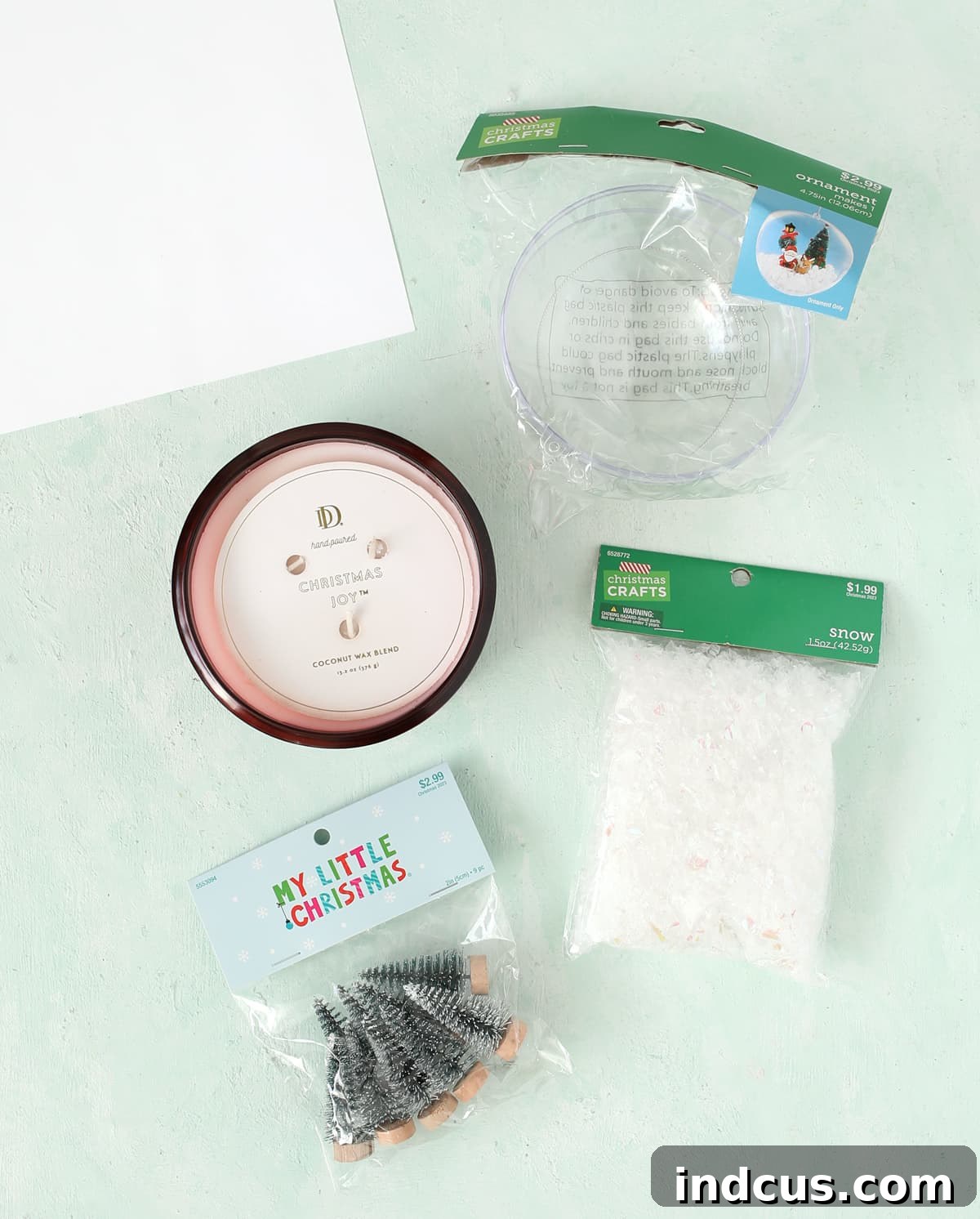 snowglobe candle diy instructions with materials like a candle, ornament, snow, and mini trees