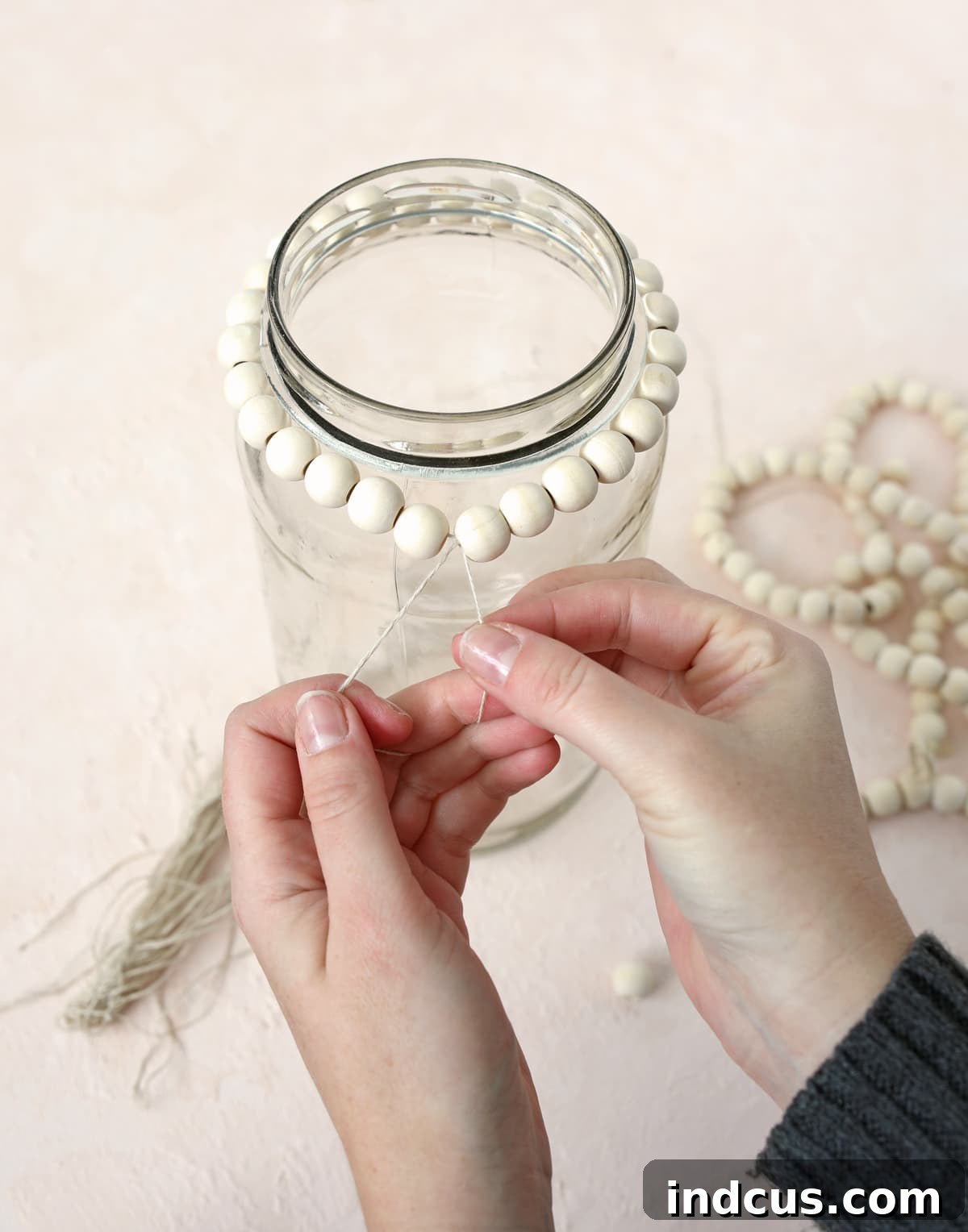 Stringing wood beads to form the top ring around a glass jar