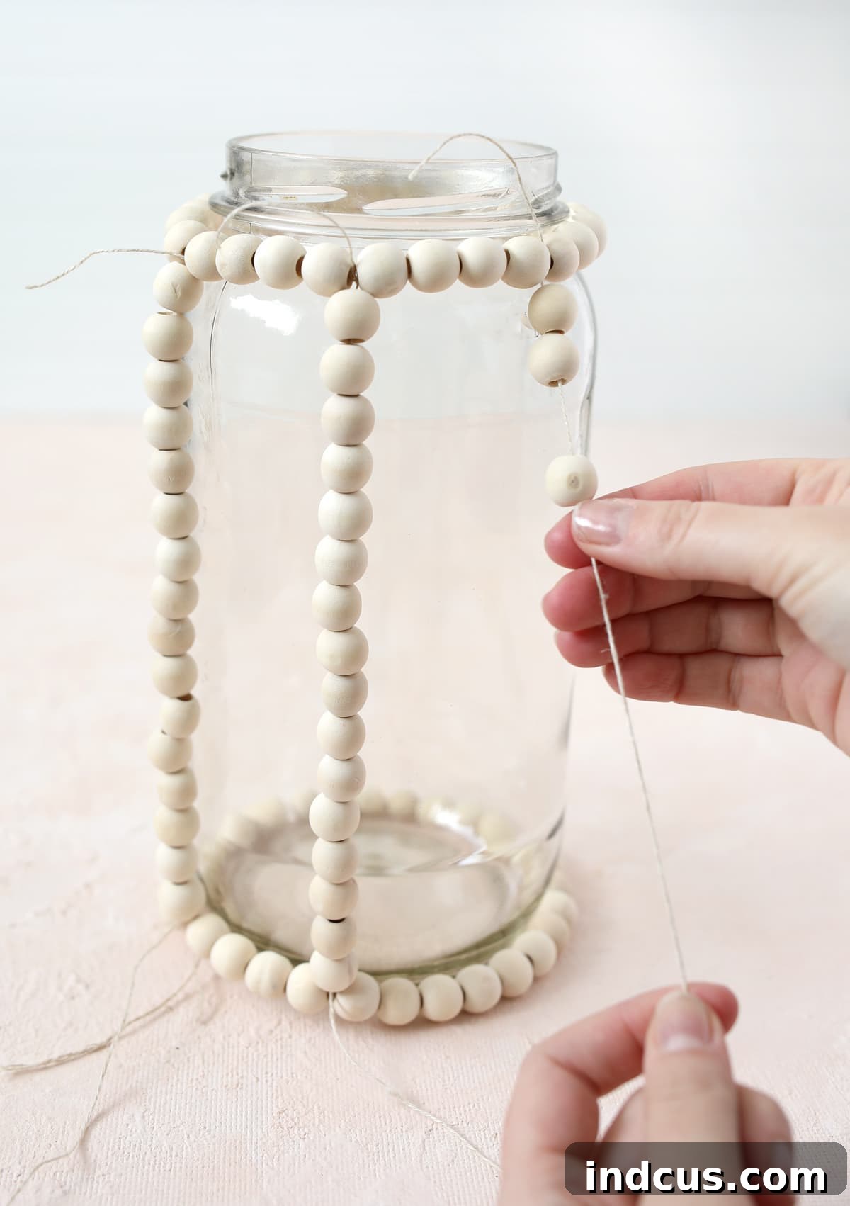 Tying wood beads to a glass jar to craft a decorative lantern