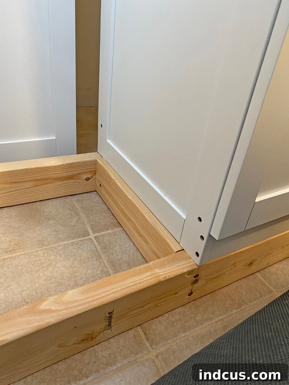 Aligning a flat-pack cabinet onto the custom 2x4 lumber base for built-in installation