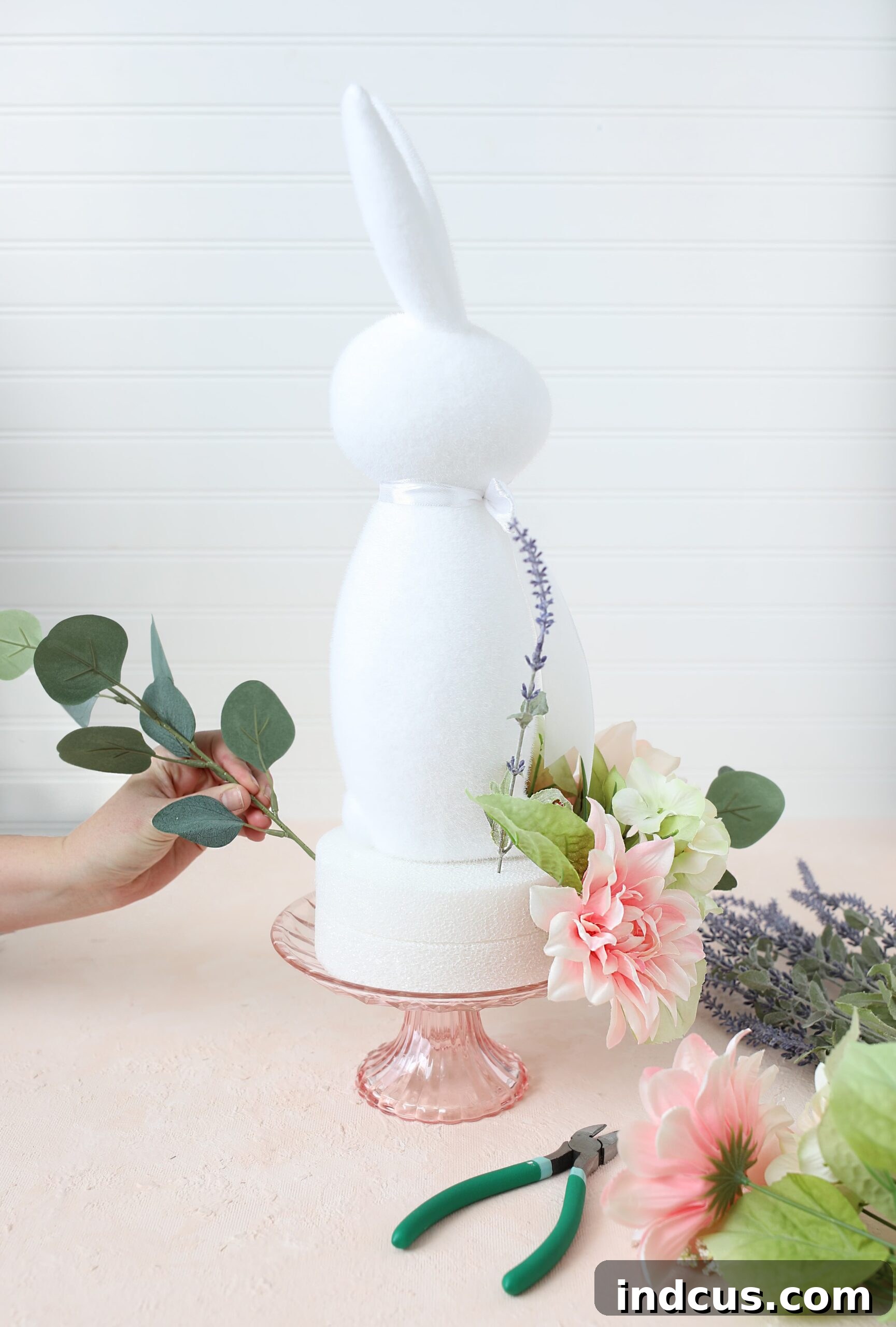 Close-up of a finished DIY floral centerpiece on a cake stand with a white bunny and pastel flowers
