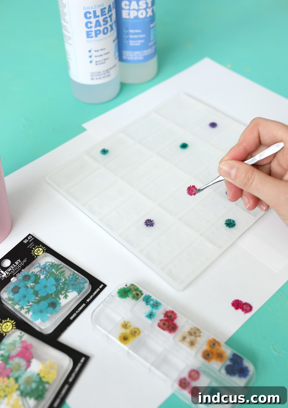 Detailed shot of tweezers gently placing tiny pressed flowers into a clear resin domino mold.