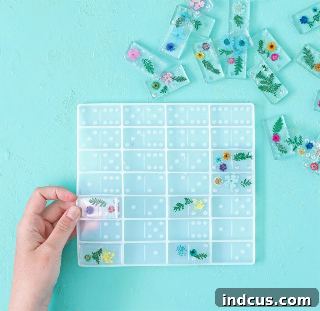 Hands carefully removing perfectly cured, clear resin dominoes from a flexible silicone mold, revealing embedded pressed flowers.