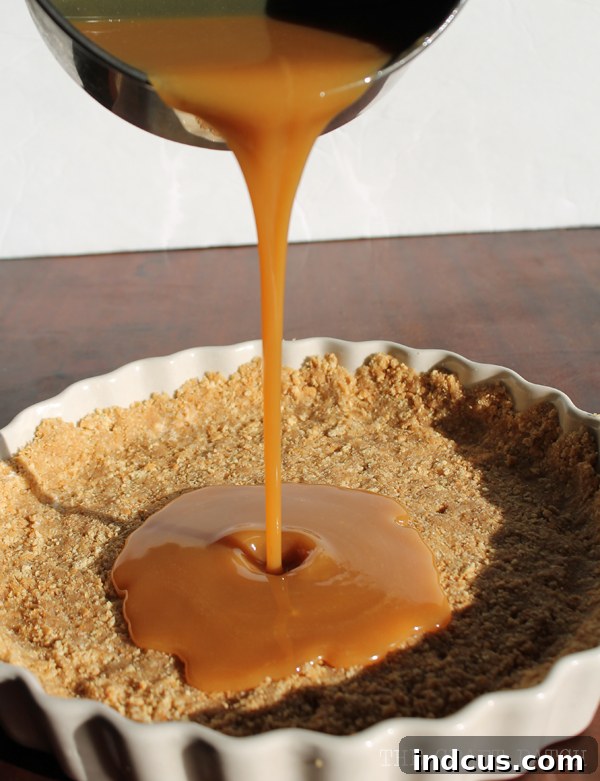 Smooth, rich caramel being generously poured into the prepared graham cracker pie crust