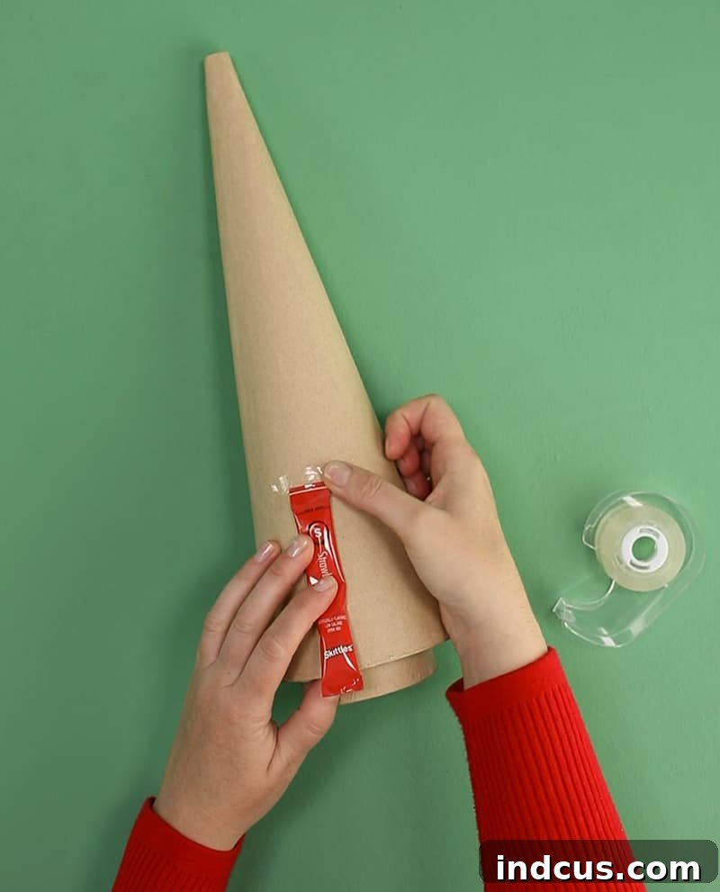 Taping the first row of drink packets onto a paper mache cone.