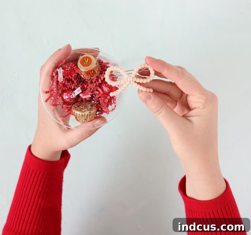 Clear plastic bowl filled with colorful shredded paper, various candies, and small gifts, ready to be transformed into a giant lollipop.
