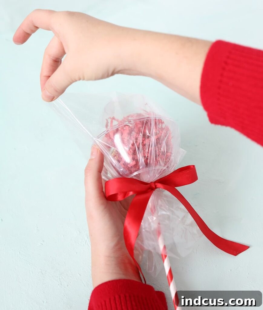 Plastic bag corners are folded down and taped neatly to create a smooth, round lollipop shape after wrapping the plastic bowls.