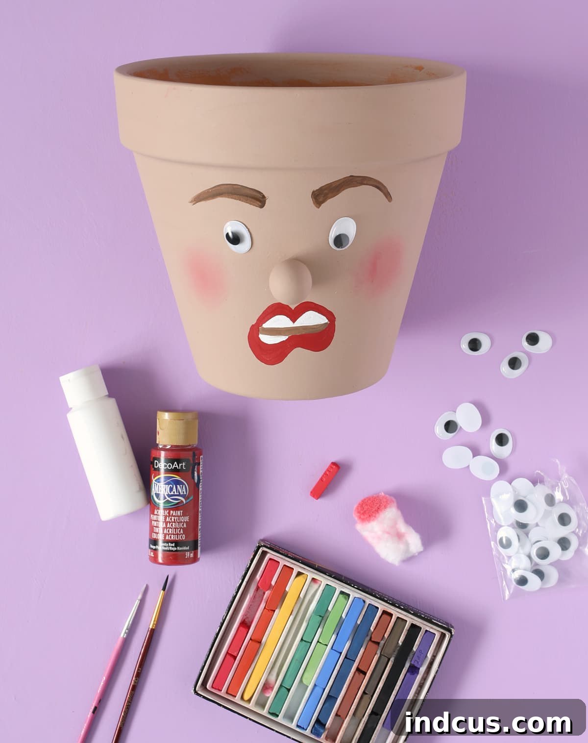 Painting a funny face on a planter with wiggle eyes and blush