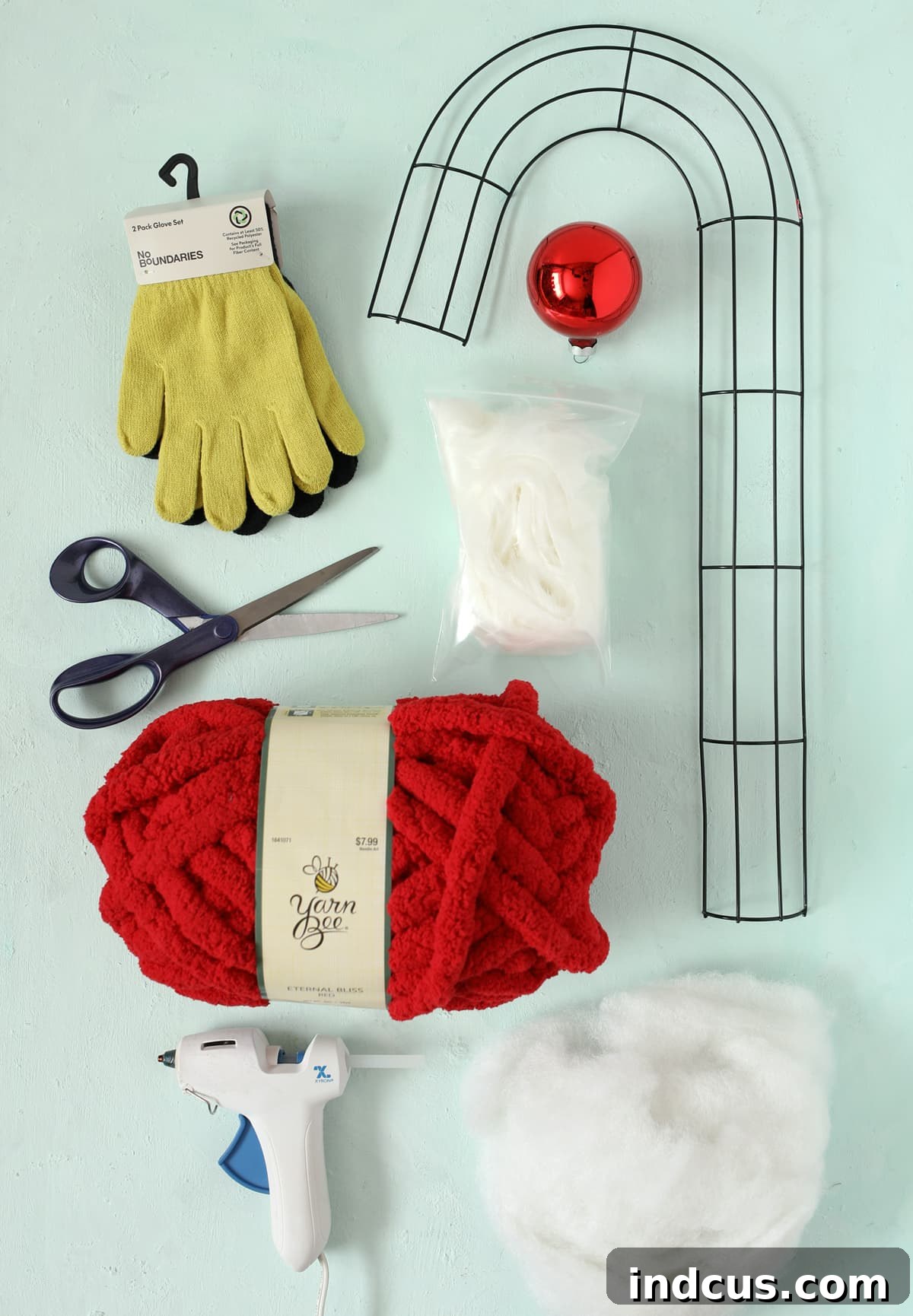 Array of crafting materials including green gloves, red yarn, wire frame, and faux fur, laid out on a white surface.