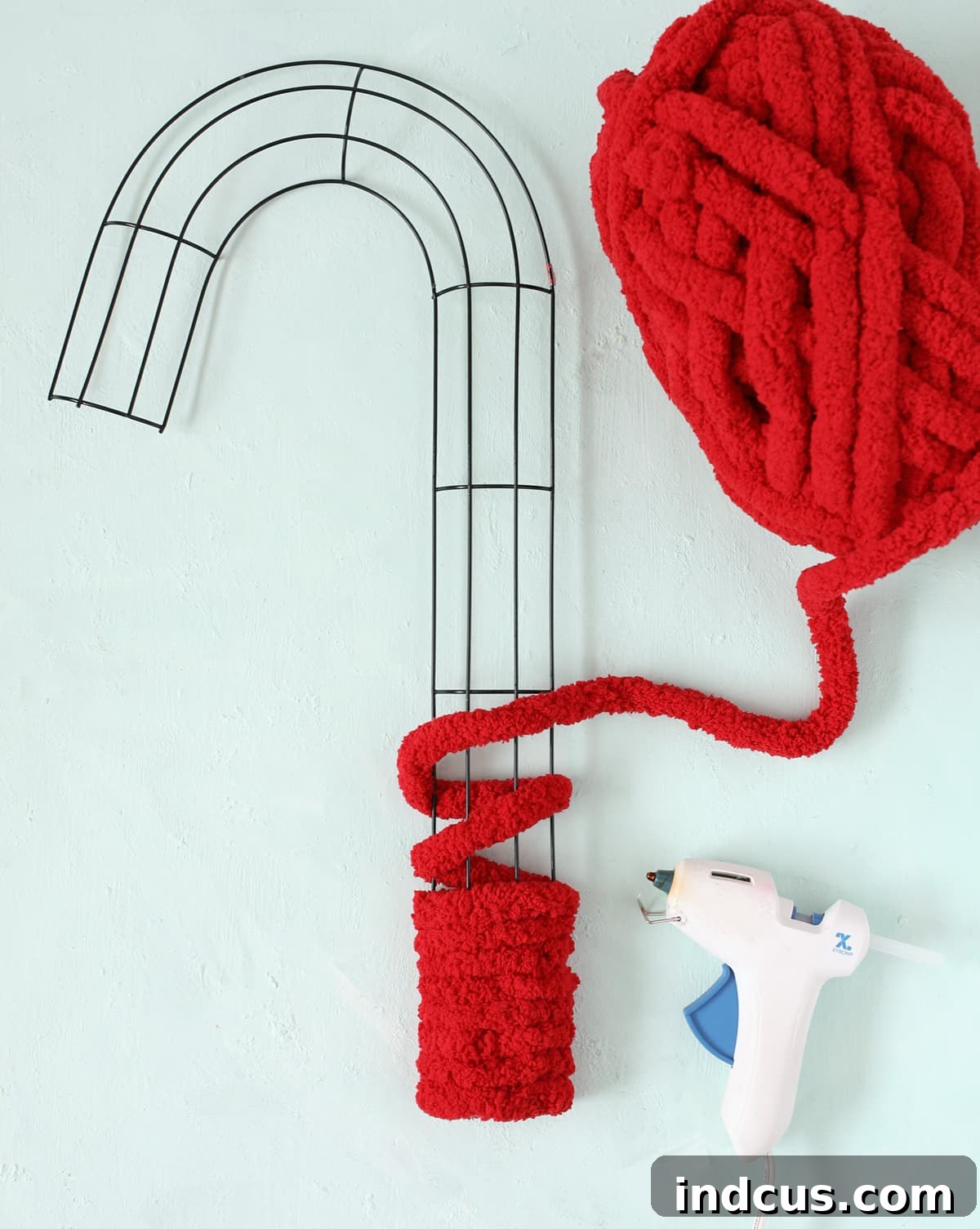 A candy cane wire wreath form being wrapped neatly with bright red yarn.