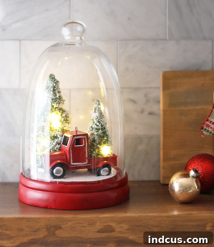 A charming red truck Christmas cloche, featuring miniature winter scene with bottle brush trees and snow.