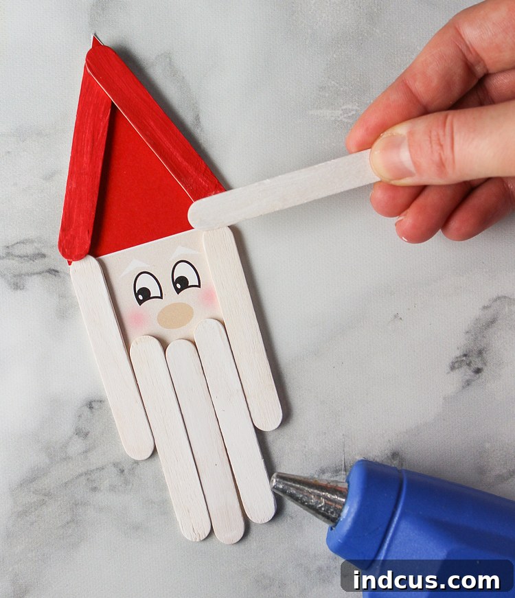 Assembling a popsicle stick Santa ornament with glue and cardstock