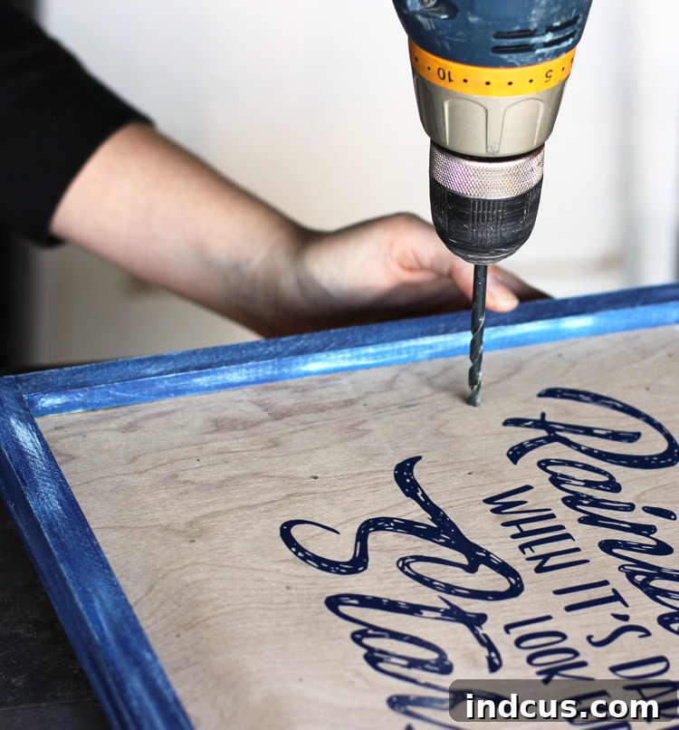 A person drilling holes into a wooden sign with a pencil mark, demonstrating how to make a lighted wooden sign carefully.