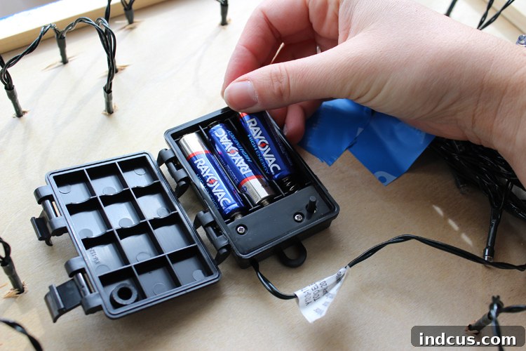 The back of a DIY lighted sign showing a short strand of battery-operated lights and the battery pack secured with tape.