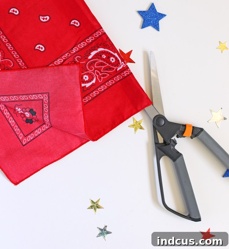 Close-up view of a bandana being cut in half, demonstrating the preparation for making fabric strips.