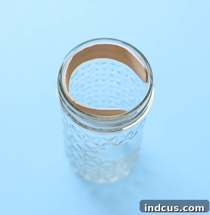 A softened popsicle stick bent and placed inside a glass jar to hold its curved shape.