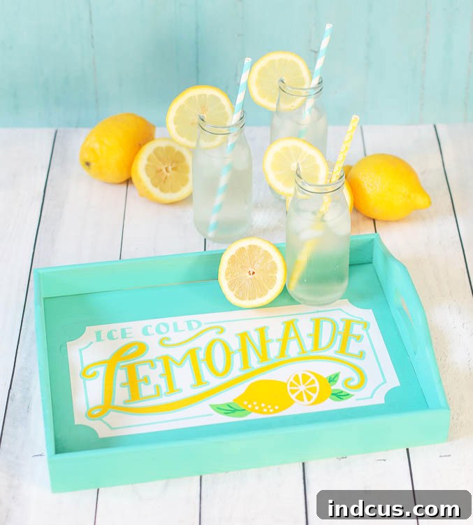 A beautifully crafted wooden serving tray adorned with a vibrant 'Lemonade' design made from adhesive vinyl. The tray holds glasses of iced lemonade and lemon slices, set against a bright, summery background.
