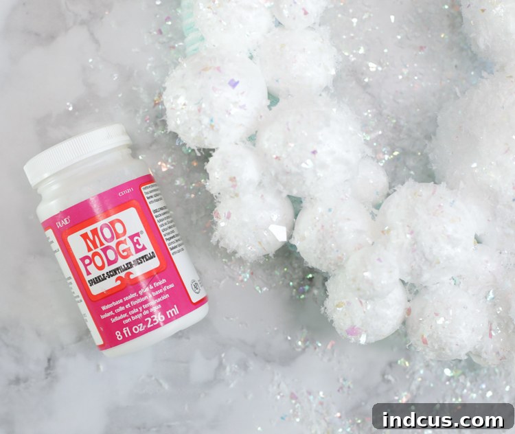 Applying Mod Podge and glitter snow to foam balls for a winter wreath.