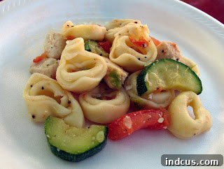 A vibrant bowl of tortellini with chicken, zucchini, and tomato, garnished with fresh Parmesan cheese and herbs, ready to be served.