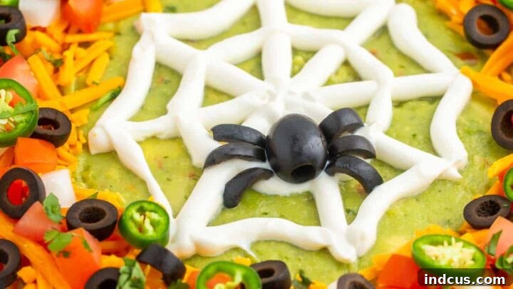 Layered Halloween taco dip decorated with a sour cream spiderweb.
