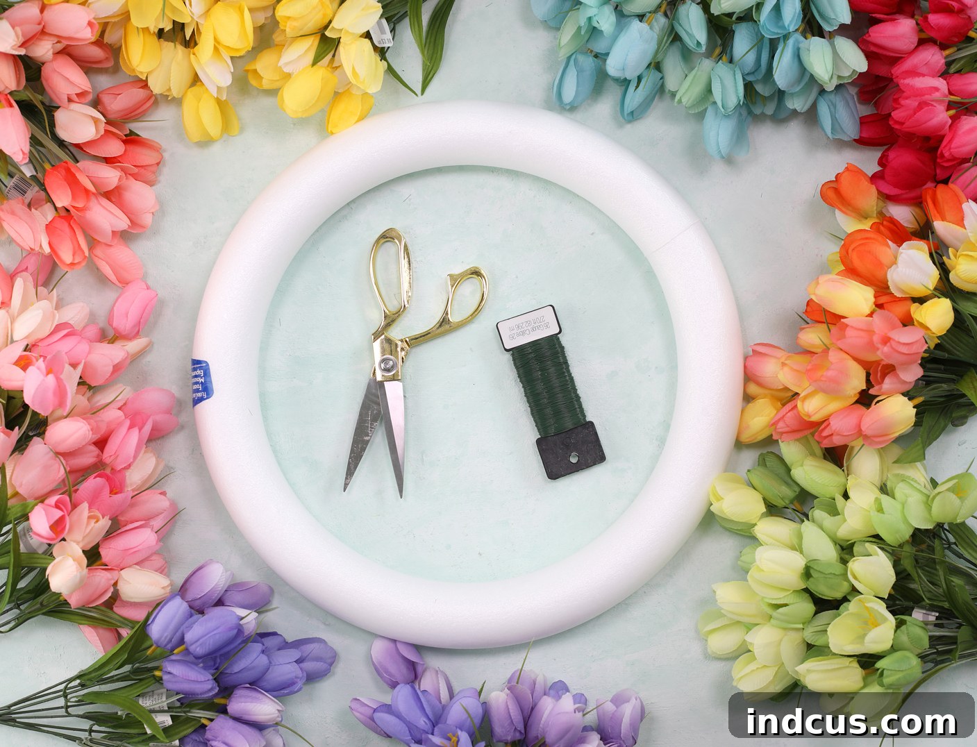 Various craft supplies laid out on a table for making a tulip wreath, including colorful tulip bunches and a foam wreath form