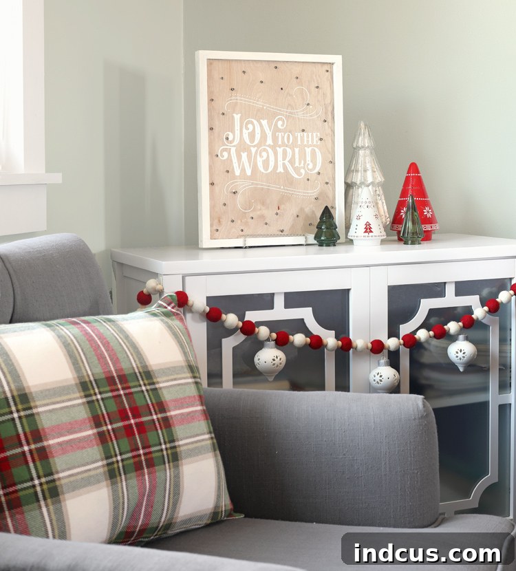 Yuletide Charm: Inside Festive Homes 17 Living room Christmas decor with a DIY lighted sign, ceramic trees, and a customized felt ball garland.